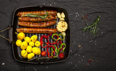 Wiener Sausages with vegetables and spices in a pan on black backgroundの写真素材