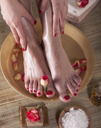 Female feet and hands with spa bowl, flowers, sea salt and bar soap on wooden background. Foot spa concept.の写真素材