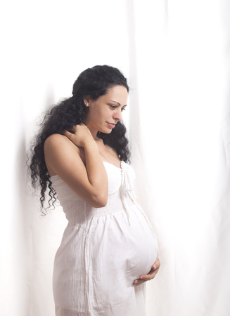 Portrait of a pregnant young woman with white dress on a white background.の写真素材