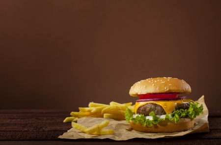 Fresh delicious burger with beef, tomato, cheese, onion and lettuce on wooden table and brown...