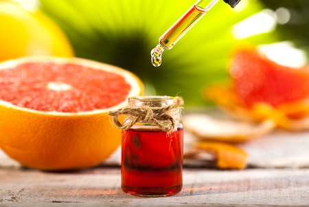 Bottle of essential oil from grapefruits on wooden table and green leaves background - alternative medicineの写真素材