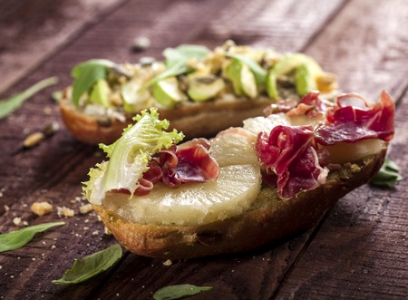 Closeup of bruschettas with avocado, mascarpone, rucola nuts, prosciutto and pineapple on a wooden...