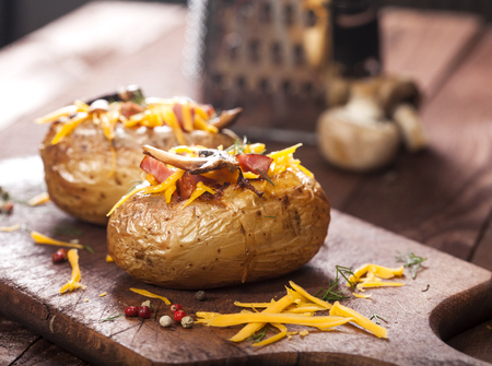 Baked stuffed potatoes with bacon, cheddar, mushrooms and dill on wooden tableの写真素材
