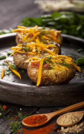 Baked stuffed potatoes with cheese, bacon, chives, dill and spices on dark backgroundの写真素材