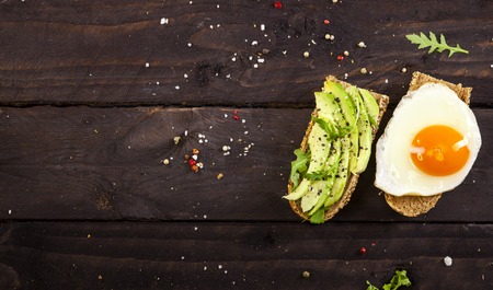Closeup of two different bruschettas with avocado, rucola sesame, seeds, egg on a wooden table.の写真素材