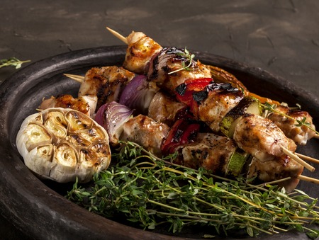 Grilled chicken skewers with spices and vegetables in a pan on a dark background. Front view and closeupの写真素材