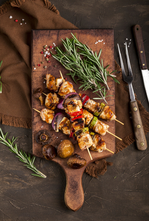 Grilled chicken skewers with spices and vegetables on a cutting board and dark background. Top view.の写真素材