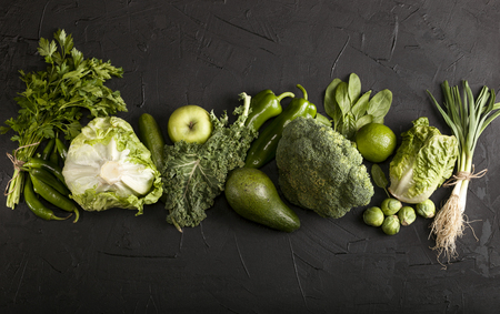 Green health food fruits and vegetables. Kale leaves broccoli cucumber lime apple kiwi avocado lettuce brussels sprouts parsley hot pepper chilli garlic chives green onion cabbage baby spinach peas dill. Copy space and top view on black background. Raw, vegan, vegetarian, alkaline food concept. Banner.の写真素材