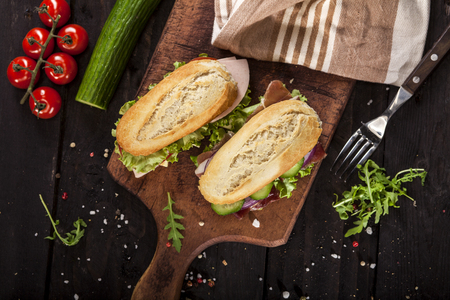 Fresh delicious burgers with cheese, tomato, onion, ham, prosciutto, cucumber and lettuce on wooden table and dark background. Top viewの写真素材