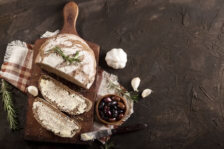 Sliced traditional toast bread with butter, olives, garlic and herbs on a cutting board, napkin and...