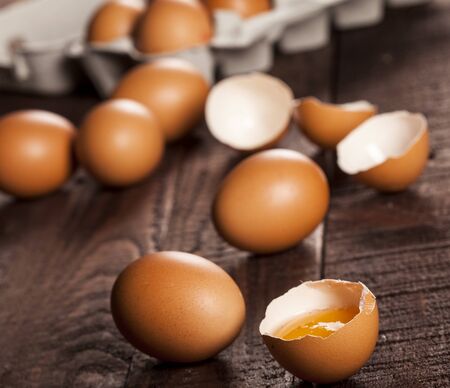 Brown eggs in a box and broken egg with yolk on dark rustic table background.