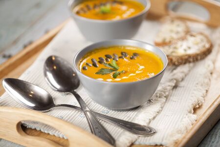 Delicious creamy pumpkin and carrot vegetable soup with seeds, bread and parsley close-up on blue background.の写真素材
