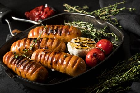 Sausages with thyme and vegetables in a pan on a black background.の写真素材