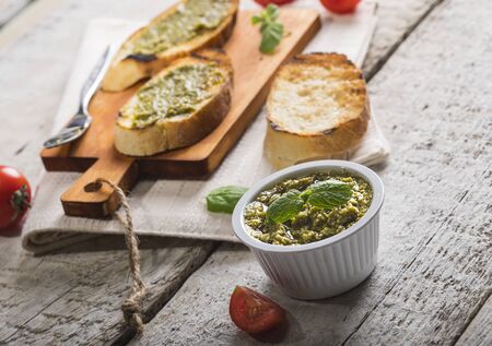 Sliced traditional toast bread with pesto, cherry tomato and basil on a cutting board and white wooden table. Top view.の写真素材