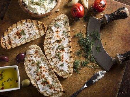 Sliced traditional toast bread with cream cheese, olives, garlic and herbs on a cutting board and dark table. Top view.の写真素材