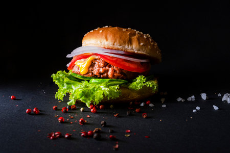 Delicious hamburger with beef, tomato, cheese, lettuce, onion and sauce on black backgroundの写真素材