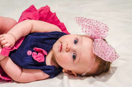 Portrait of a baby girl in a dress with diapers with a bow on her head which lies on the bedの写真素材