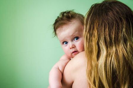 Naked girl smiling baby on the shoulder of mothers with long hair on a green backgroundの写真素材
