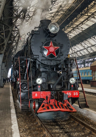 LVIV, UKRAINE - DECEMBER, 2015: Old Soviet vintage black retro train with a red star at the railway station in Lviv produces steam from the pipes and the passengers waiting on the landing Peronのeditorial素材