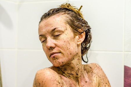 Face of young beautiful sexy girl with long hair girl who takes a bath naked in the spa procedures, wellness dealt a protective mask of coffee for skin healthの写真素材