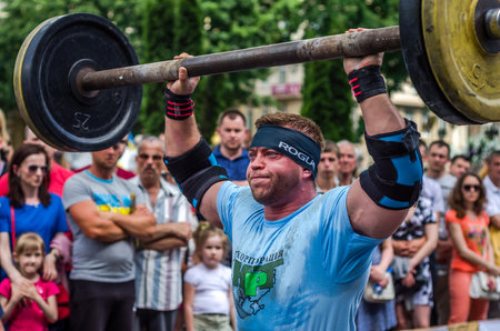 LVIV, UKRAINE - JUNE 2016: Athlete strongman inflated with athletic body lifting heavy barbell on a city streetのeditorial素材
