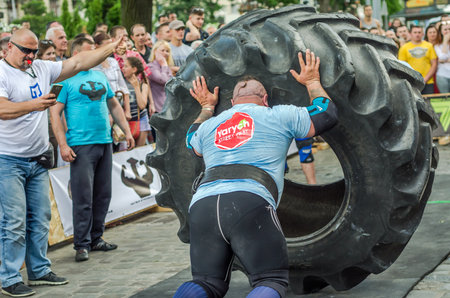 LVIV, UKRAINE - JUNE 2016: Strong bodybuilder athlete, the athlete rolls the wheel of a huge black Goodyear from the truck on the street in front of the amazed publicのeditorial素材