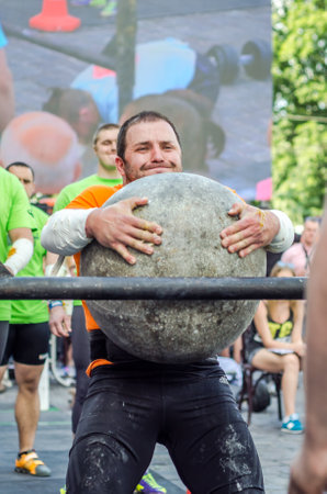 LVIV, UKRAINE - JUNE 2016: Strong bodybuilder strongman lifts a huge heavy stone ball made of marble and throws it over the bar on the street under the eyes of stunned spectatorsのeditorial素材