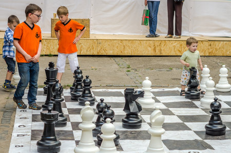 LVIV, UKRAINE - JUNE 2016: Young children, the future grandmasters play on a chess board chess exercising outdoors huge figuresのeditorial素材