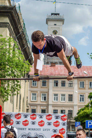 LVIV, UKRAINE - JUNE 2016: Young boy athlete demonstrates his ability by performing different exercises and figures on the horizontal bar on the city streets, promoting sport and a healthy lifestyleのeditorial素材