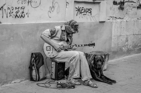 LVIV, UKRAINE - AUGUST 2016: Street musician playing rock hits of the electric guitar, sitting with a large black dog, near the walls of the house with graffiti on the old streets of Lvivのeditorial素材