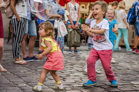 LVIV, UKRAINE - AUGUST 2016: Young children catching soap bubbles in the city, playing, joyful and radiating positive emotions, happy childrenのeditorial素材