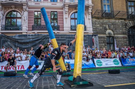 LVIV, UKRAINE - AUGUST 2017: A strong bodybuilder athlete lifts a huge steel pipe to the strongman game in front of enthusiastic spectatorsのeditorial素材