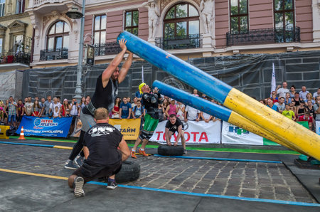 LVIV, UKRAINE - AUGUST 2017: A strong bodybuilder athlete lifts a huge steel pipe to the strongman game in front of enthusiastic spectatorsのeditorial素材
