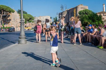 ROMA, ITALY - JULY 2017: A small charming tourist girl skates on a scooter along the streets of ancient Rome near the Colosseumのeditorial素材