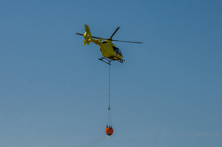 ROMA, ITALY - JULY 2017: A fire helicopter is picking up the water in a basket for extinguishing a...