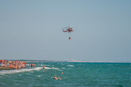 ROMA, ITALY - JULY 2017: The firefighter helicopter during the rescue operation collects water in the Tyrrhenian Sea and extinguishing the fire by eliminating the natural disaster in Ostia, Italyのeditorial素材