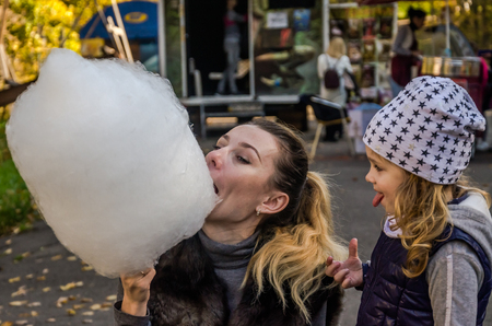 A little girl with her mama is eating a huge cotton candy in an amusement park - a happy familyの写真素材