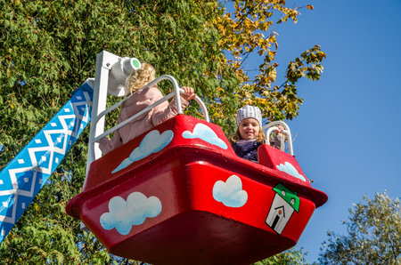LVIV, UKRAINE - OCTOBER 2017: Little children, charming girls girlfriends ride in an amusement park on a swingのeditorial素材