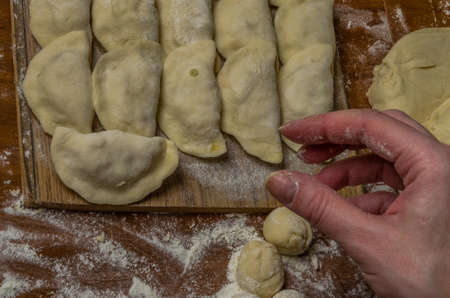 The hands of a woman cook cooked on a table of flour dough and make varenikiの写真素材