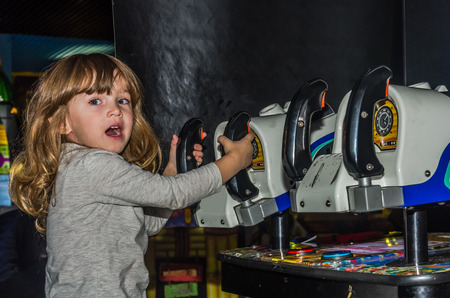 Little charming girl the child goes for a ride in an amusement park on the carousel and plays video simulatorsの写真素材