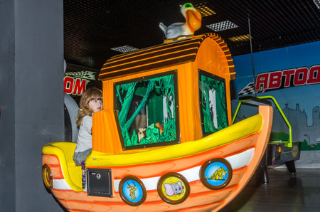 LVIV, UKRAINE - NOVEMBER 2017: Little charming girl the child goes for a ride in an amusement park on the carousel and plays video simulatorsのeditorial素材