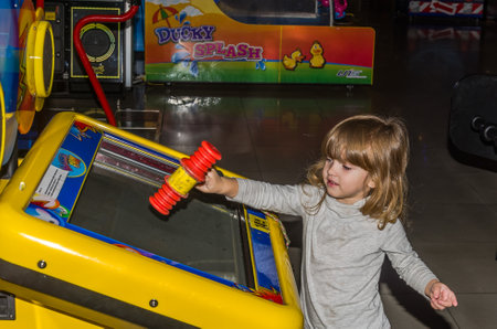 LVIV, UKRAINE - NOVEMBER 2017: Little charming girl the child goes for a ride in an amusement park on the carousel and plays video simulatorsのeditorial素材
