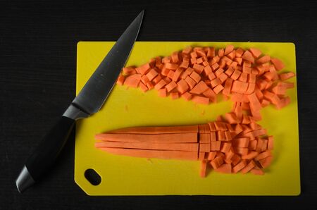 Carrot cut with knife for cooking on a yellow cutting board on a dark backgroundの写真素材