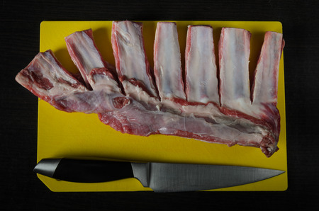 Meat lamb ribs cut with a knife on a yellow cutting board on a dark backgroundの写真素材