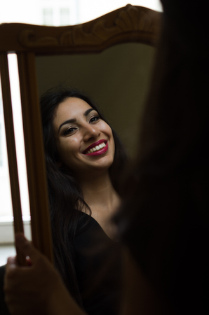 Young charming brunette girl looks at her reflection in the mirrorの写真素材