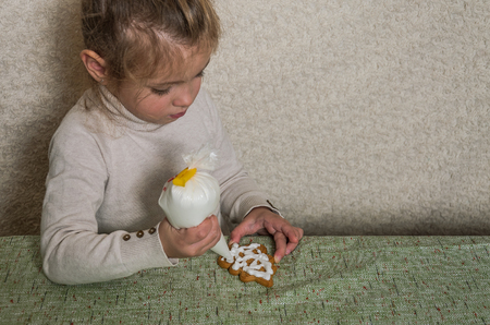 Little charming girl decorates New Year's gingerbread with white sugar icingの写真素材