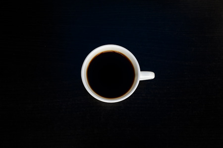 White cup of coffee on a black table, top view