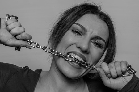 Young beautiful girl bites the chain with her teeth, trying to figure it outの写真素材