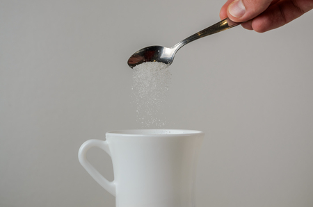 A hand spooning sugar in a white mugの写真素材