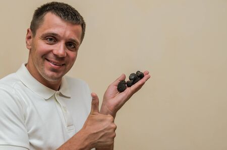 Young guy holding black truffle mushrooms in his hands on a light backgroundの写真素材